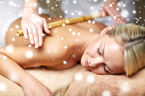 people, beauty, spa, winter and relaxation concept - close up of beautiful young woman lying with closed eyes and having bamboo back massage in spa with snow effect