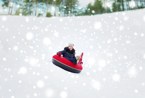 winter, leisure, sport, and people concept - happy teenage girl or woman sliding down on snow tube