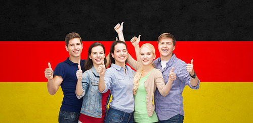 education, nationality, gesture and people concept - group of smiling friends or students standing and showing thumbs up over german flag background