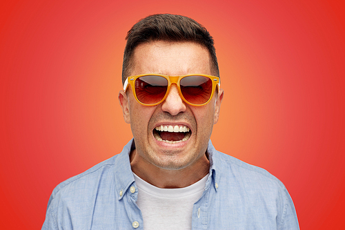 emotions, negative, fashion and people concept - face of angry middle aged latin man in shirt and sunglasses over red background
