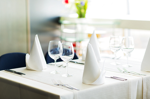 objects, dinnerware and holidays concept - close up of table setting with glasses, napkins and cutlery