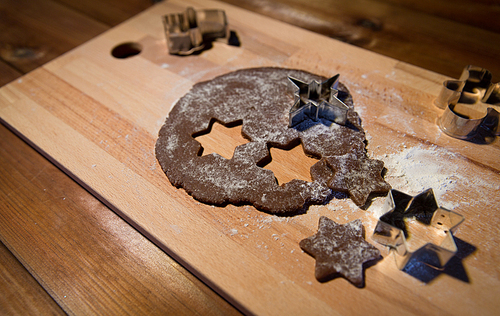 baking, cooking, christmas and food concept - close up of gingerbread dough, molds and flour on wooden cutting board from top