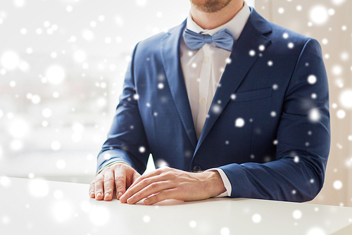 people, fashion, style and wedding concept - close up of best man or groom in suit and bow-tie at table with falling snow effect