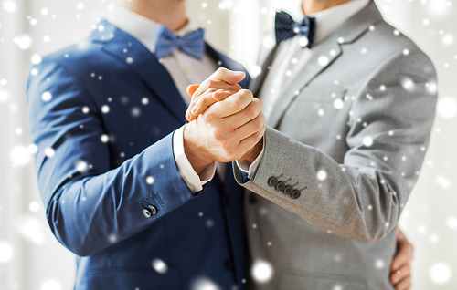 people, homosexuality, same-sex marriage and love concept - close up of happy male gay couple holding hands and dancing on wedding over snow effect