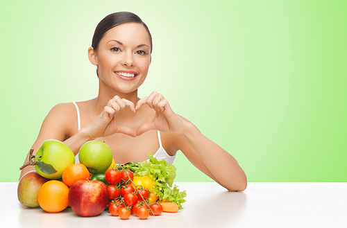 people, food, diet, healthy eating and weight loss concept - happy beautiful woman with fruits and vegetables showing heart shape hand sign over green background