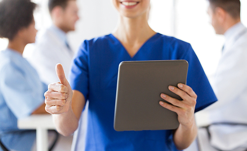 technology, gesture, health care, people and medicine concept - close up of happy female doctor or nurse with tablet pc computer over group of medics showing thumbs up at hospital