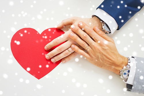 people, homosexuality, same-sex marriage, valentines day and love concept - close up of happy married male gay couple hands with red paper heart shape on table over snow effect