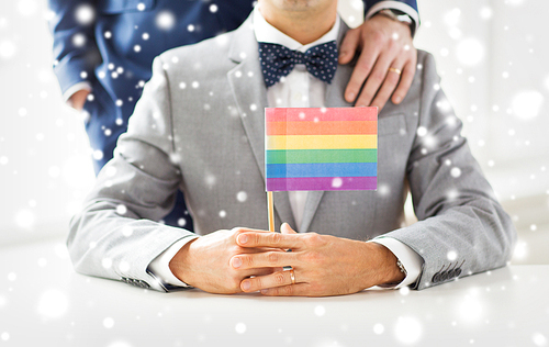 people, homosexuality, same-sex marriage and love concept - close up of happy male gay couple in suits and bow-ties with wedding ring holding rainbow flag over snow effect