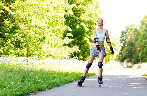 fitness, sport, summer, rollerblading and healthy lifestyle concept - happy young woman in rollerblades and protective gear riding outdoors