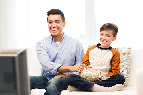 family, people, technology, television and entertainment concept - happy father and son with popcorn watching tv at home