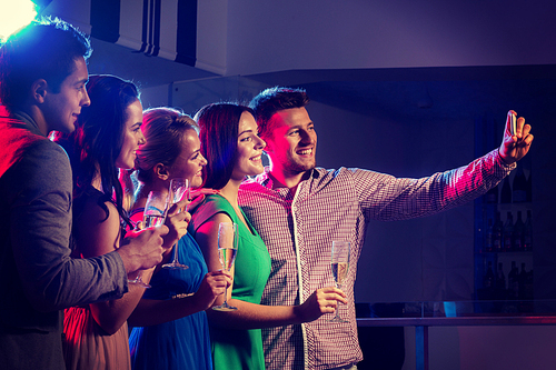 party, holidays, technology, nightlife and people concept - smiling friends with glasses of champagne and smartphone taking selfie in club