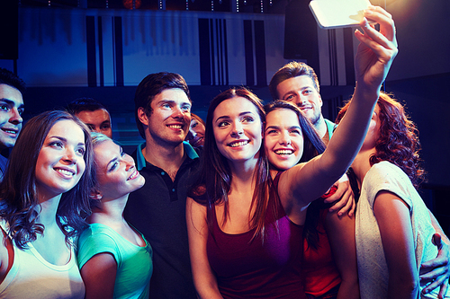 party, technology, nightlife and people concept - smiling friends with smartphone taking selfie in club