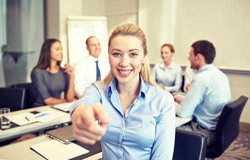 business, people and teamwork concept - smiling businesswoman pointing finger up with group of businesspeople meeting in office