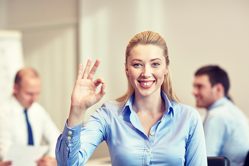 business, people and teamwork concept - smiling businesswoman showing ok gesture with group of businesspeople meeting in office