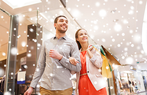 sale, consumerism and people concept - happy young couple with shopping bags walking in mall with snow effect