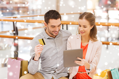 sale, consumerism, leisure and people concept - happy couple with tablet pc computer, credit card and shopping bags in mall with snow effect