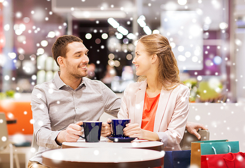 sale, shopping, consumerism, leisure and people concept - happy couple with shopping bags drinking coffee in mall with snow effect