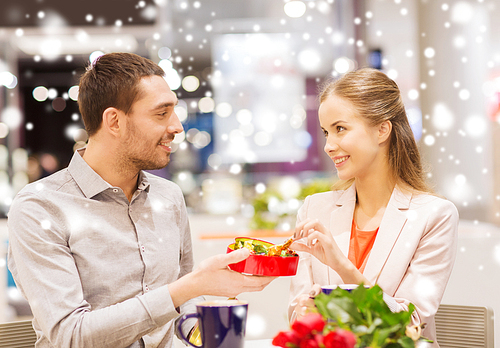 love, romance, valentines day, couple and people concept - happy young couple with red flowers and open gift box in at cafe mall with snow effect