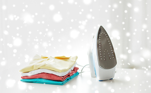 ironing, clothes, housework and objects concept - close up of iron and clothes on table at home over snow effect