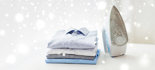 ironing, clothes, housework and objects concept - close up of iron and clothes on table at home over snow effect