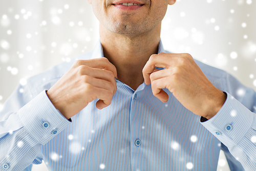 people, business, fashion and clothing concept - close up of smiling man dressing up and adjusting shirt collar at home over snow effect