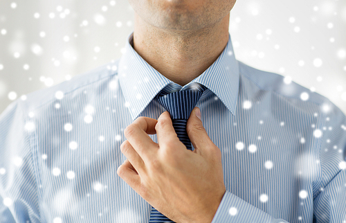 people, business, fashion and clothing concept - close up of man in shirt dressing up and adjusting tie on neck at home over snow effect