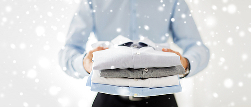 business, clothing and people concept - close up of businessman holding folded shirts over snow effect