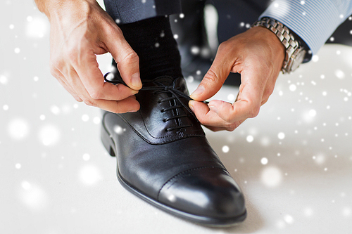 people, business, fashion and footwear concept - close up of man leg and hands tying shoe laces over snow effect