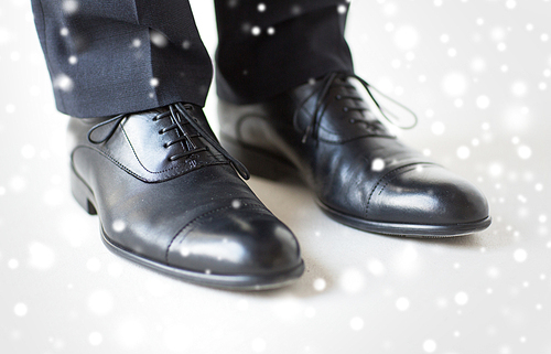 people, business, fashion and footwear concept - close up of man legs in elegant shoes with laces or lace boots over snow effect