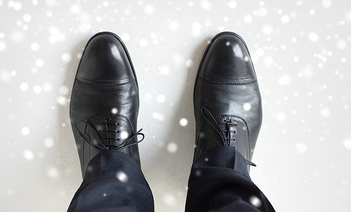 people, business, fashion and footwear concept - close up of man legs in elegant shoes with laces or lace boots over snow effect