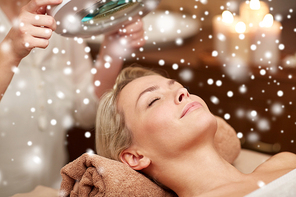 people, beauty, skin care, winter and relaxation concept - close up of beautiful young woman lying with closed eyes and beautician looking through magnifying lamp in spa salon with snow effect