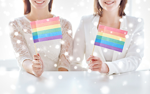 people, homosexuality, same-sex marriage, gay pride and love concept - close up of happy lesbian couple holding rainbow flags over snow effect