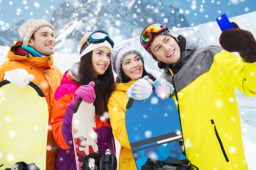 winter sport, leisure, friendship, technology and people concept - happy friends with snowboards and smartphone taking selfie over snow and mountain background