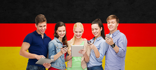 people, education and modern technology concept - smiling students using smartphones and tablet pc computer over german flag background
