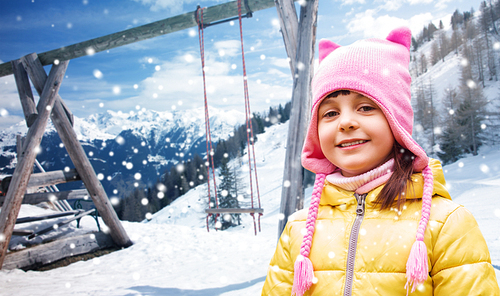 childhood, vaion, winter holidays and people concept - happy beautiful little girl portrait outdoors over swing, snow and mountains background