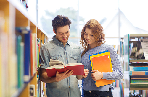 people, knowledge, education and school concept - happy student couple with books in library
