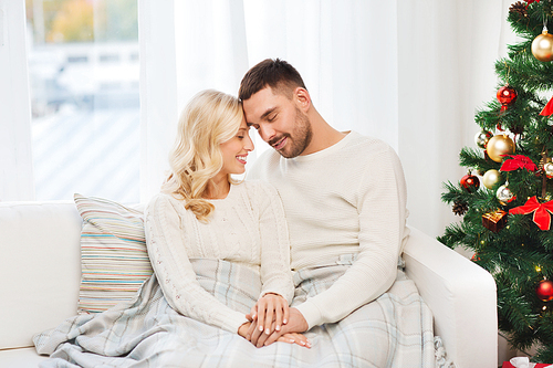 family, love, christmas, winter holidays and people concept - happy couple covered with plaid sitting on sofa at home