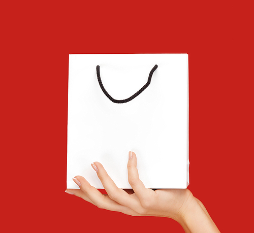 people, sale, consumerism, advertisement and commerce concept - close up of hand holding blank white bag over red background