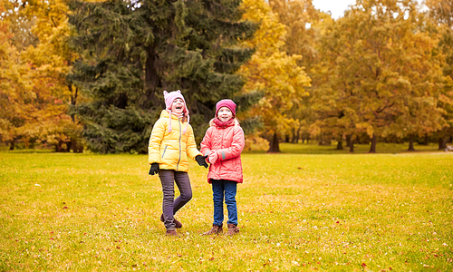 autumn, childhood, leisure and people concept - two happy little girls in park