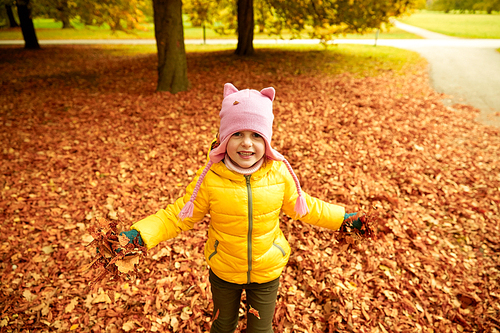 autumn, childhood, nature and people concept - happy little girl playing with fallen leaves in park