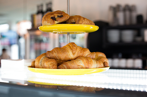 food, baking, junk-food and unhealthy eating concept - close up of croissants and buns on cake stand at cafe or bakery