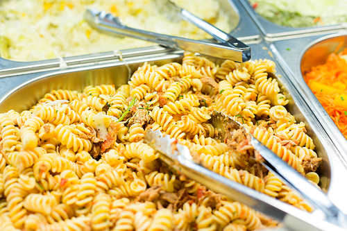 food, catering, self-service and eating concept - close up of pasta and dishes with tongs on metallic tray