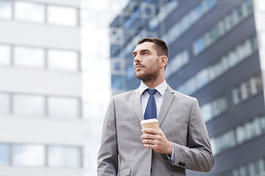 business, hot drinks and people and concept - young serious businessman with paper coffee cup over office building