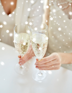 people, homosexuality, same-sex marriage, celebration and love concept - close up of happy married lesbian couple hands holding and clinking champagne glasses over snow effect