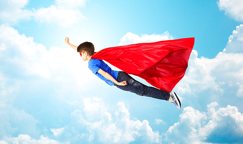imagination, freedom, childhood, movement and people concept - boy in red superhero cape and mask flying in air over blue sky and clouds background