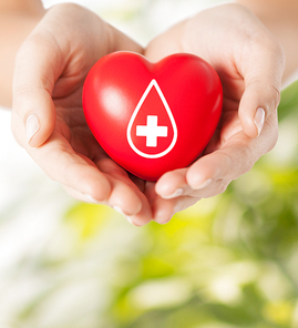 healthcare, medicine and blood donation concept - female hands holding red heart with donor sign over green natural background