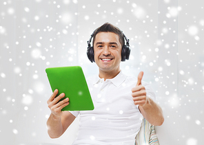 technology, people, lifestyle and distance learning concept - happy man with tablet pc computer and headphones listening to music and showing thumbs up at home over snow effect