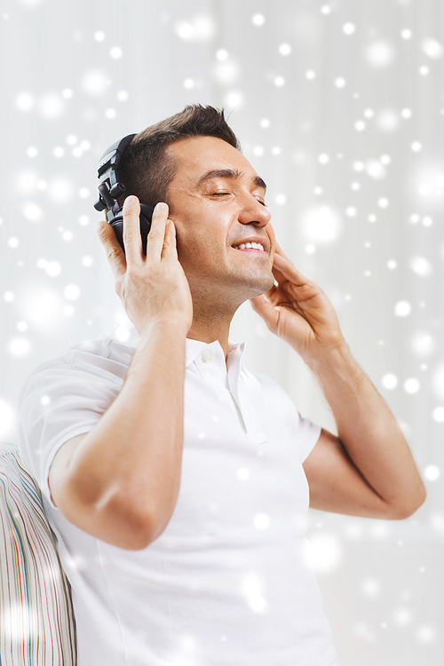 technology, people and lifestyle concept - happy man in headphones listening to music at home over snow effect