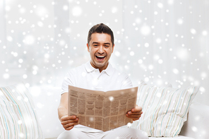 leisure, information, people and mass media concept - happy man reading newspaper and laughing at home with snow effect