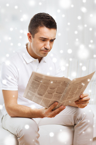 leisure, information, people and mass media concept - sad man reading newspaper at home with snow effect